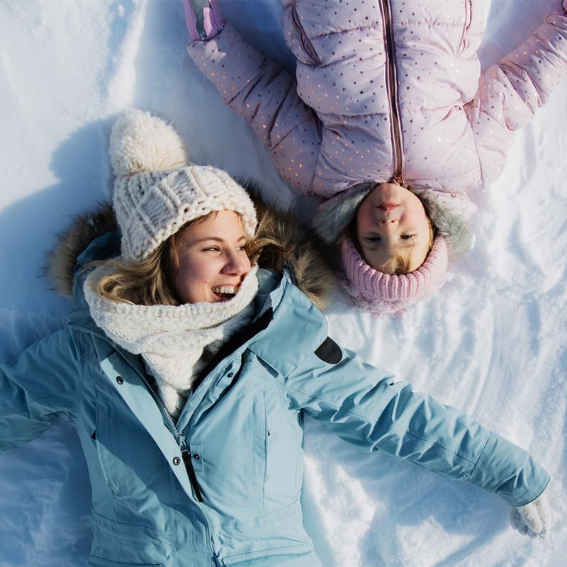 A woman and child making snow angels in the mountainous snow